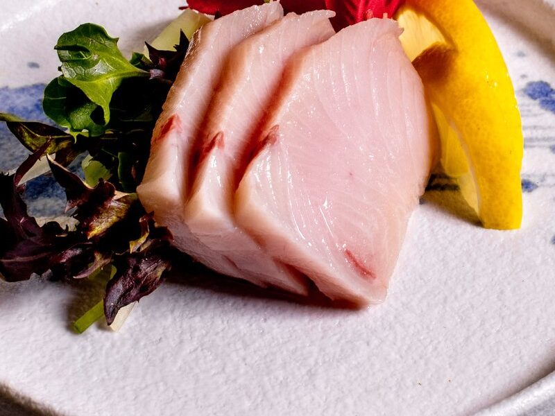 Yellowtail sashimi with greens and a lemon wedge